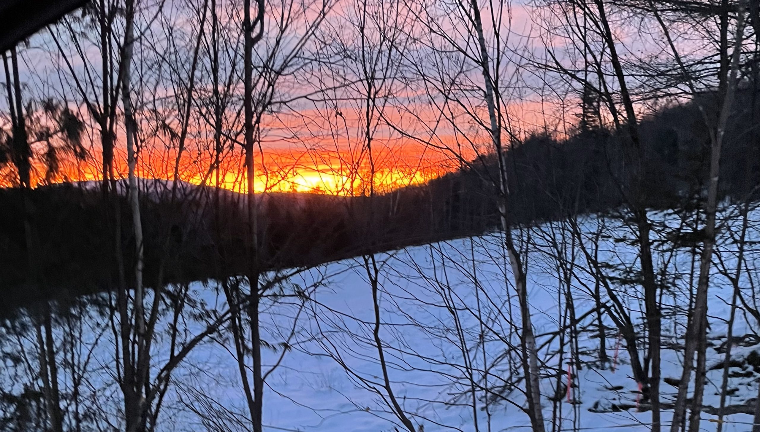 picture of sunrise over distant mountains with snowy clearing in foreground
